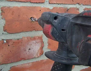 A close up of a driller on a brick wall.