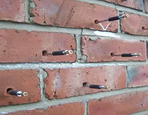 A brick wall with a bunch of screws attached to it.