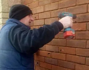 A man using a drill gun on a brick wall.